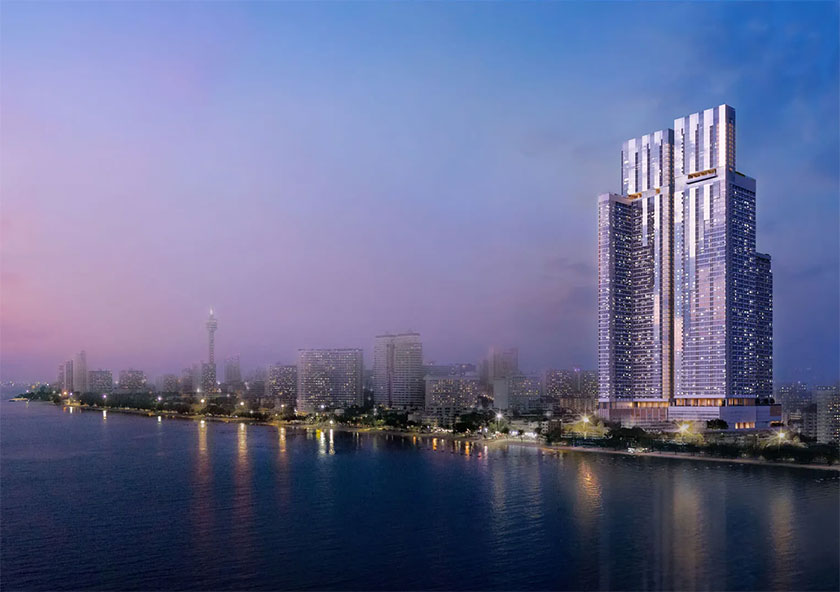 Skypark Lucean Jomtien Pattaya | Skyscraper towers over a twilight cityscape by a tranquil waterfront, illuminated against a purple-hued sky.